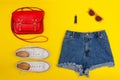 Denim shorts, white sneakers, red handbag. Bright yellow background. Fashionable concept Royalty Free Stock Photo