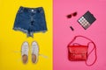 Denim shorts, white sneakers, red handbag, cosmetics. Bright yellow and pink background. Fashionable concept Royalty Free Stock Photo