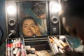 DENPASAR/BALI-MAY 11 2019: Balinese woman applying make up for a evening performance in front of a mirror in the makeup room.