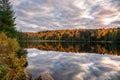 Dense forest and cloudy sky reflectiong in the calm waters of a lake at sunset