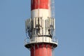 Densely installed multiple cell phone antennas and transmitters on tall white and red industrial chimney surrounded with metal Royalty Free Stock Photo