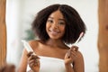 Dental care. Attractive young black woman with radiant smile holding toothpaste and brush in front of mirror at home Royalty Free Stock Photo