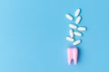 Dental care concept. Toothache pills. Pink tooth model and medical tablets on a blue background with copy space. Close up view of