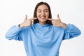 Dental clinic and people concept. Young woman smiling, pointing fingers at white perfect straight teeth, advertising