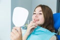Dental clinic. Reception, examination of the patient. Teeth care. Young girl smiling, looking in the mirror after a