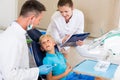 Dentist with assistant are diagnosticating to young patient which is sitting