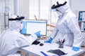 Dentist assistant in ppe suit pointing at patient waiting list