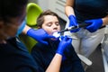 Dentist and assistant treats teeth to teenager. Doctor filling cavity of the boy using ultraviolet lamp.