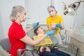 The dentist with assistent showing the little boy how to clean the teeth with a toothbrush on an artificial jaw dummy.