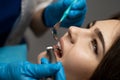 Dentist in blue gloves filling the beautiful smiling woman patient`s root canal using mirror and drill in clinic close up, Royalty Free Stock Photo