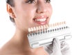 Dentist checking young woman`s teeth color on white background