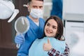 Dentist female showing her patient`s new teeth through the mirror in the dental cabinet. Patient is satisfied and showing thumb u Royalty Free Stock Photo