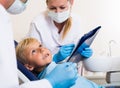 Dentist with girl assistant are diagnosticating to young patient which is sitting