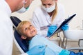 Dentist guy with female assistant are diagnosticating to young patient which is sitting