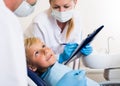 Dentist guy with girl assistant are diagnosticating to young patient which is sitting