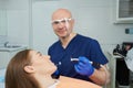 A dentist holds a dental mirror and a drill near a patient in the dental chair