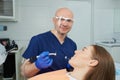 A dentist holds a dental mirror and a drill near a patient in the dental chair