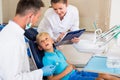 Dentist man with assistant are diagnosticating to young patient which is sitting