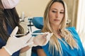 Dentist prepares anesthesia in dental office out of focus background of blonde patient looking at injection