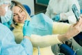 The dentist in a protective mask sits next to the patient and takes a photo after work