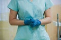 Dentist`s office. The dentist`s gloved hands are folded and the doctor is standing in a special blue medical uniform. Equipment