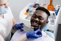 Dentist showing teeth color shades guide for tooth whitening for african patient in dental clinic. African is looking at Royalty Free Stock Photo