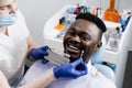 Dentist showing teeth color shades guide for tooth whitening for african patient in dental clinic. African is looking at Royalty Free Stock Photo