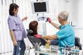 Dentist team, senior man dentist and his female assistant, in dental office talking with female patient and preparing Royalty Free Stock Photo