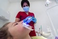 The dentist uses an ultraviolet lamp while fitting the girl with braces