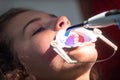 The dentist uses an ultraviolet lamp while fitting the girl with braces