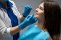 Dentist wearing blue gloves examines smiling woman patient using dental scaler while she is sitting half a turn in dental chair in