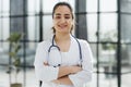 Dentist woman standing with crossed arms. Confident dentist standing in a hospital corridor in a white coat.