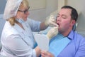 Dentist woman is teaching man to clean teeth using dental floss in dentistry.