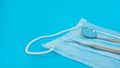 Dentistry Tools: Sickle Probe And Mouth Mirror Lying On Protective Blue Face Mask