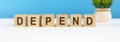 depend word made with wooden blocks on white desk, blue background