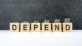 depend word, text written on wooden cubes on a black background with coins on cubes