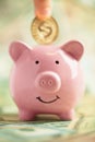 Depositing gold coin in smiling pink Piggy bank on piles of money. Saving money concept Royalty Free Stock Photo