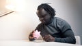 Depresed African american black man shaking empty piggy bank.