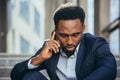 Depressed african american businessman telling sad news talking on cell phone sitting on office stairs in business suit Royalty Free Stock Photo