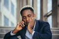 Depressed african american businessman telling sad news talking on cell phone sitting on office stairs in business suit Royalty Free Stock Photo