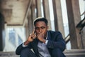 Depressed african american businessman telling sad news talking on cell phone sitting on office stairs in business suit Royalty Free Stock Photo