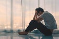 Depressed caucasian man losing job and heartbroken at same time sitting alone near window in dark at evening time with low light Royalty Free Stock Photo