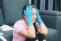 Depressed crying woman looks stressfully, keeps both hands on head, wears protective gloves, feels fatigue of busy day and