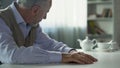 Depressed elderly man sitting at kitchen table, widower suffering loneliness