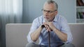 Depressed ill man in his 50s sitting on couch, putting hands on walking stick Royalty Free Stock Photo