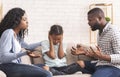 Depressed little black girl sitting between arguing parents, closing ears