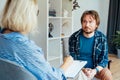 Depressed male patient having psychotherapy session with counselor at mental health clinic. Man with emotional problems Royalty Free Stock Photo