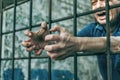 A depressed man holds his hands on the prison bars. Prisoner for the crime. Poor conditions.