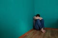 Depressed man sits in a corner in an empty green room with his head in his lap. Royalty Free Stock Photo