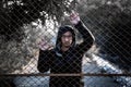 Depressed man wearing a black hoodie standing behind a fence han Royalty Free Stock Photo